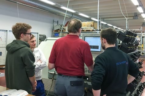 An employee explains something on a machine to three young people